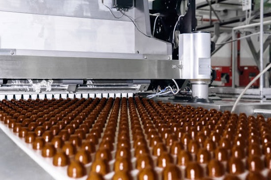 rows of toppings for chocolates manufactured by machine, on a conveyor of a chocolate factory