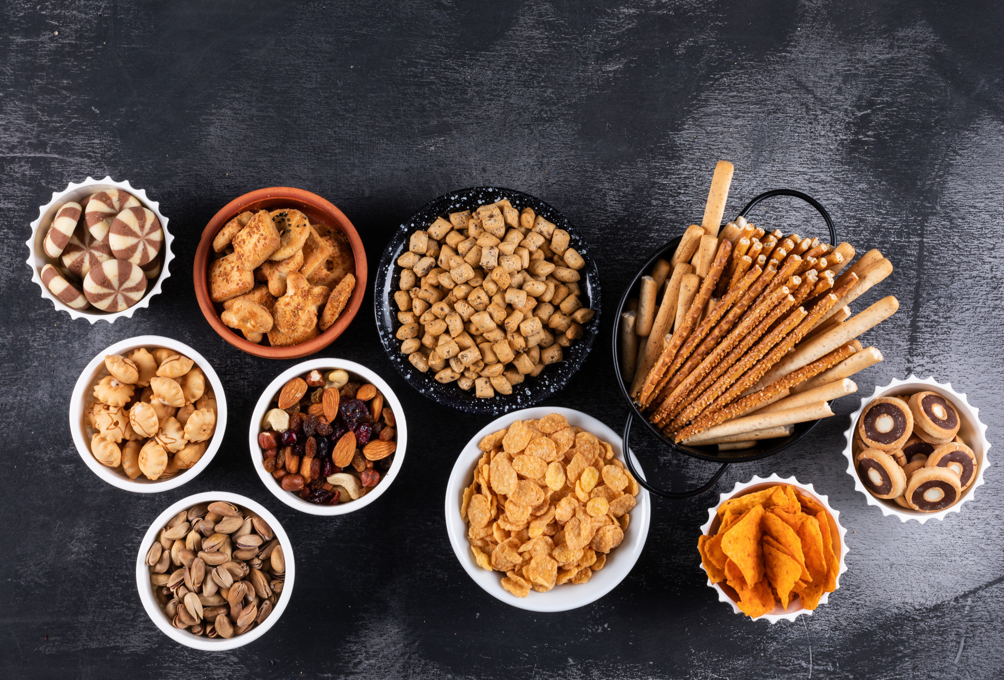 side-view-different-kind-snacks-as-nuts-crackers-cookies-bowls-with-copy-space-dark-surface-horizontal